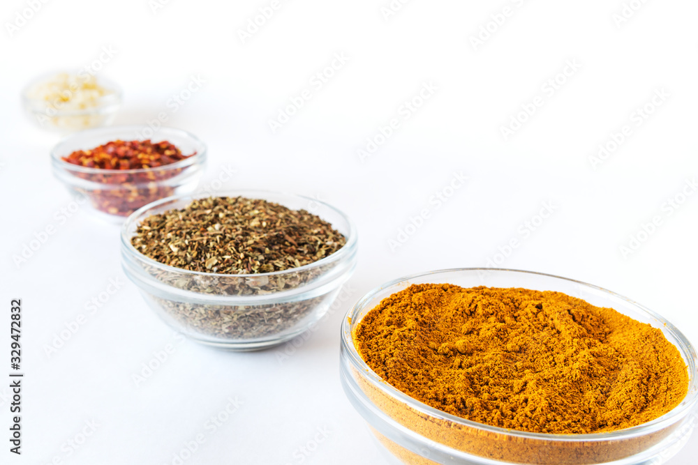 various spices in glass bowls on white background. Culinary Concept with curry, italina herb mix, crushed pepper and garlic various spices in glass bowls on white background. Culinary Concept with curry, italina herb mix, crushed pepper and garlic