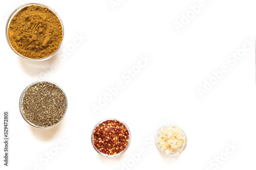 various spices in glass bowls on white background. Top view copy space. Culinary Concept with curry, italina herb mix, crushed pepper and garlic