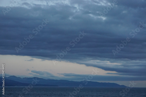 Islands and distant snow-capped mountains viewed from a cruise ship in the Gulf of Alaska, on a misty morning at sea.