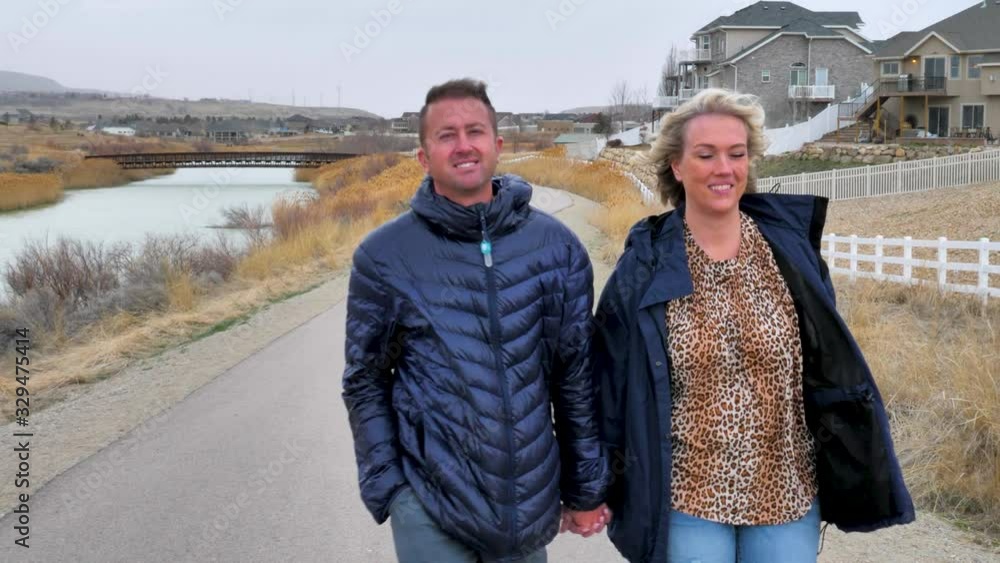 An attractive couple walks along a neighborhood nature trail holding