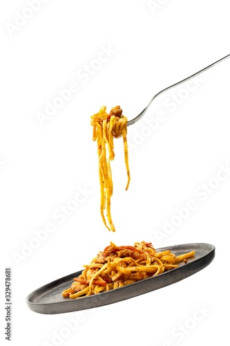 Pasta flying with fork and black plate. Isolated on white background. Illusions of levitation and falling. Classic pasta recipe.