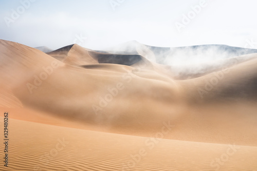 Top of a massive sand dune emerging from a thick cloud of fog after sunrise. Liwa desert, Abu Dhabi, United Arab Emirates.