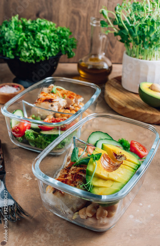 Healthy meal prep containers with chickpeas, chicken, tomatoes, cucumbers and avocados. Healthy lunch in glass containers on beige rustic background. Zero waste concept. Selective focus.