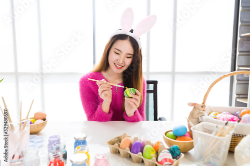 Easter holiday concept, Happy Asian Young woman wearing bunny ears hand painted eggs for Easter with colorful Easter eggs In the white room background