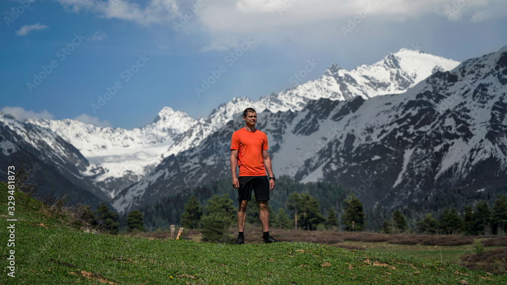 Naklejka premium The guy standing on a mountain with a green meadow sticking out veins on the hands and feet on the background of snow
