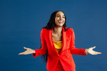 Portrait of a very happy young smiling woman in red business suit with arms out, isolated on blue background