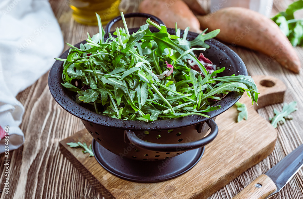 Fresh organic arugula leaves in black colander. Arugula or rucola for salad on wooden rustic background. Zero waste concept. Selective focus Fresh organic arugula leaves in black colander. Arugula or rucola for salad on wooden rustic background. Zero waste concept. Selective focus