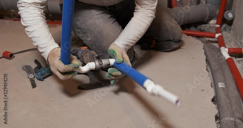 Male plumber welds plastic pipes, sewer, repair in bathroom, professional at work, pipes for supplying cold water, blue noise insulation, delicate work, heat treatment of plastic, pipes in floor