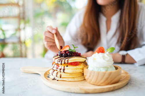 A woman eating a mixed berries pancakes with ice cream and whipped cream by wooden spoon