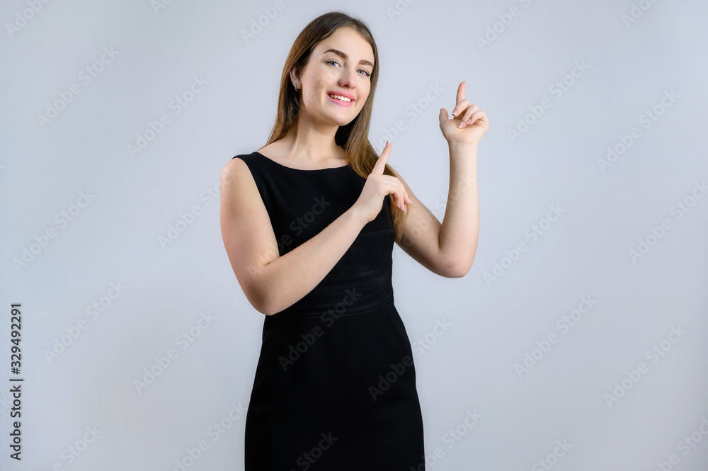 Portrait on a white background of a sympathetic Caucasian woman in a black dress shows fingers to the sides with a smile Portrait on a white background of a sympathetic Caucasian woman in a black dress shows fingers to the sides with a smile