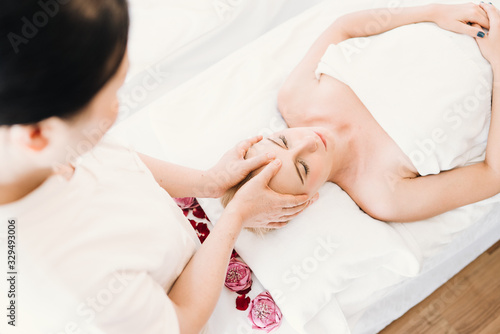 Beautiful caucasian woman having a facial massage treatment in spa salon with the hands of a therapist as a foreground, selective focus, concept spa and beauty, facial spa treatment, esthetic spa.