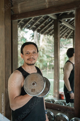 Asian young man doing exercise with lifting weights at firness house photo