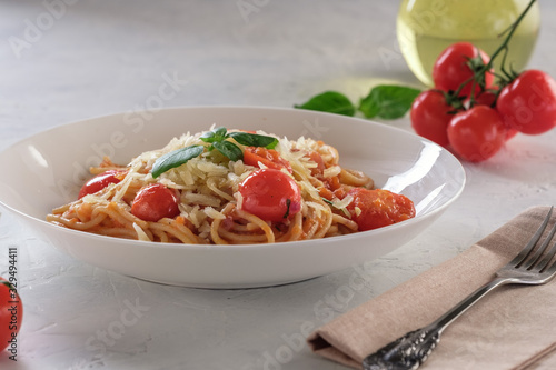 Spaghetti in tomato sauce with cherry tomatoes and basil on a white plate on a light background