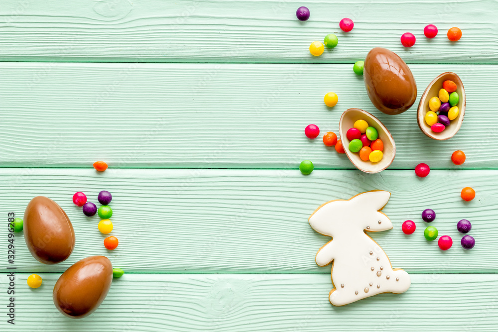 Easter sweets frame. Chocolate eggs and bunny gingerbread on green wooden background top-down frame copy space