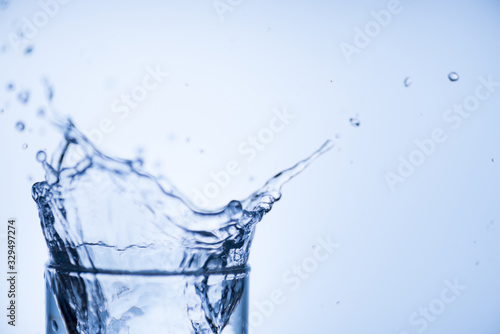 Cropped close up image of glass top full of tasty fresh clear drinkable tap water with high splash isolated over light blue white background with blank place for text