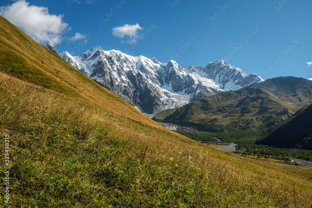 Blue clear sky sunny day big mountains with snow green slope with grass Svaneti Georgia