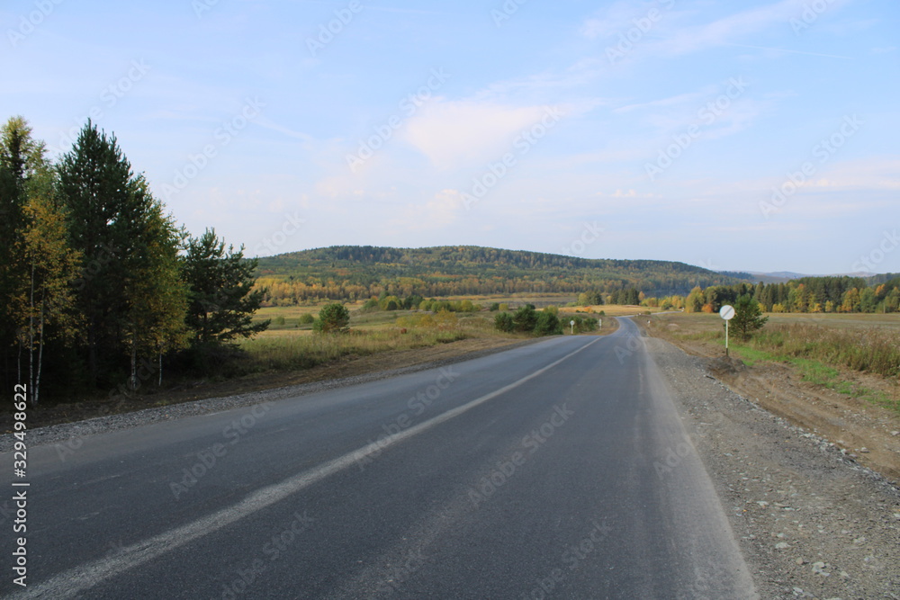 A winding road leading into the distance among multicolored clouds under a bright blue sky with white clouds.