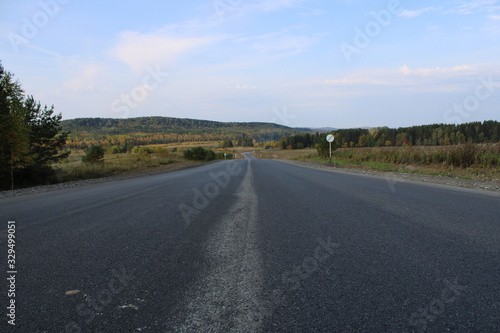  The road leading into the distance among the multicolored from the bright blue sky with white clouds
