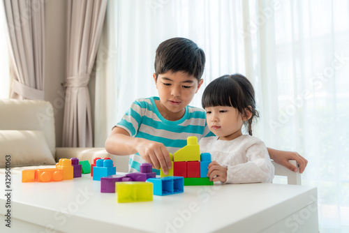 Asian cute brother and sister play with a toy block designer on the table in living room at home. Concept of bonding of sibling, friendship and learn through play activity for kid development.