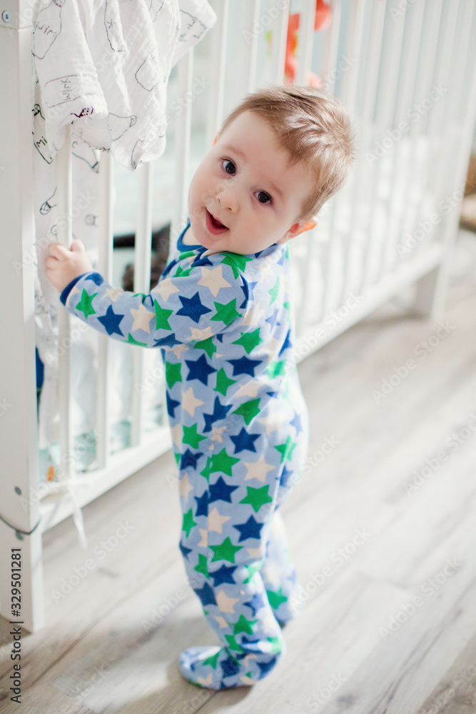 Little baby boy standing near his crib in light room Little baby boy standing near his crib in light room