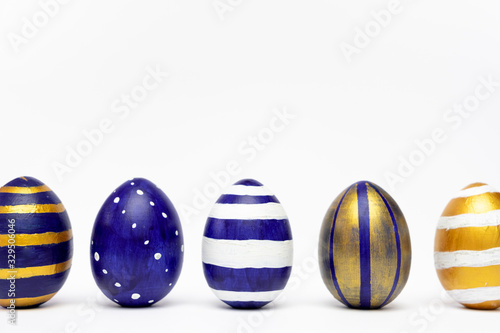 Five easter eggs trendy colored classic blue, white and golden decorated on white table. Happy Easter card with copy space for text. Minimal style.