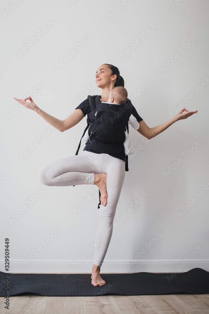 Obraz premium Young mother doing yoga with baby in ergo backpack
