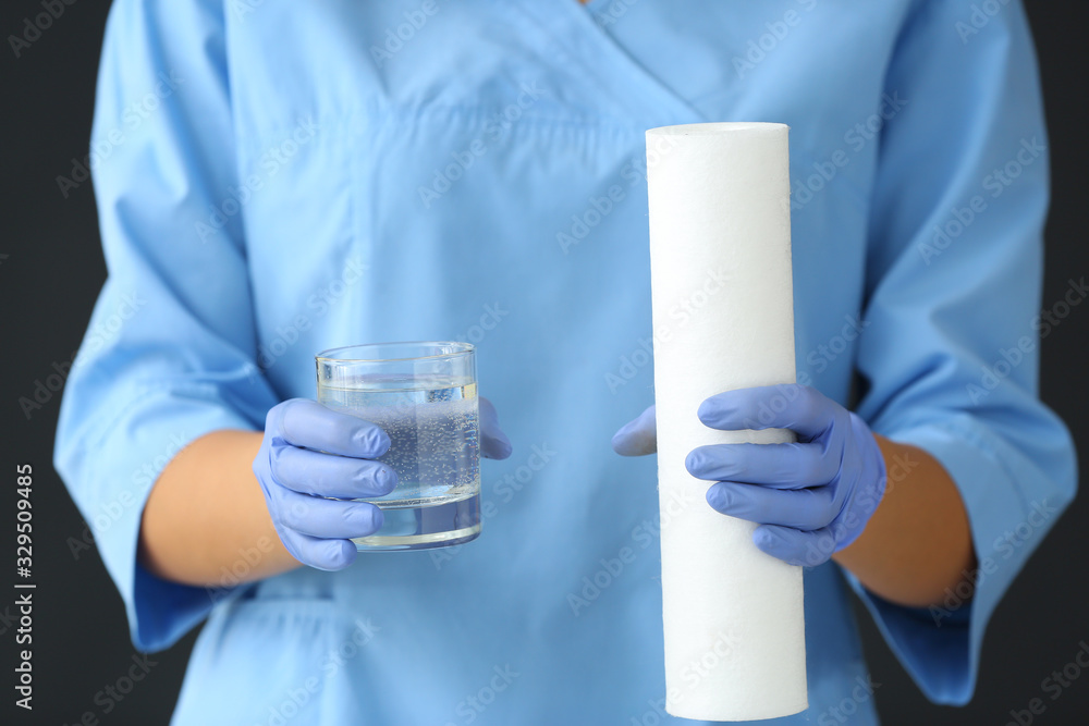 Fototapeta premium Female doctor with glass of clean water and filter on dark background, closeup