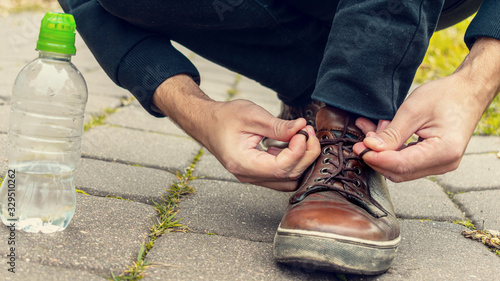 Sportsman tying shoelaces, fallen yellow leaves, water bottle, man's legs, close-up, 16:9