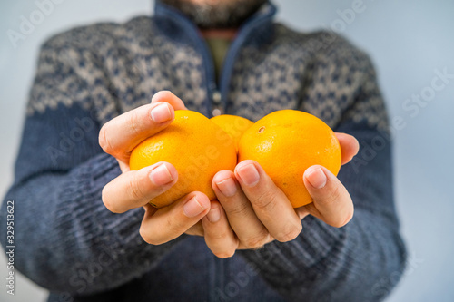 Man in the vintage sweater offering oranges, hands detail, blurred background, shallow debt of field