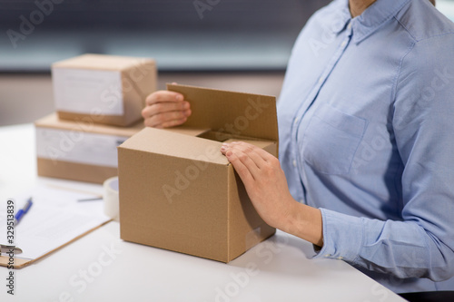 delivery, mail service, people and shipment concept - close up of woman packing parcel box at post office