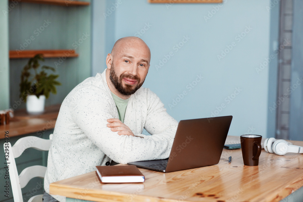 An adult attractive man working at a computer in the kitchen. A stylish person enjoys success in business. Work online. Business portrait An adult attractive man working at a computer in the kitchen. A stylish person enjoys success in business. Work online. Business portrait
