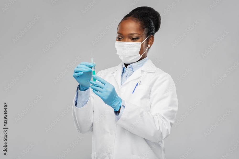 medicine, vaccination and healthcare concept - african american female doctor or scientist in mask with syringe over grey background - obrazy, fototapety, plakaty 