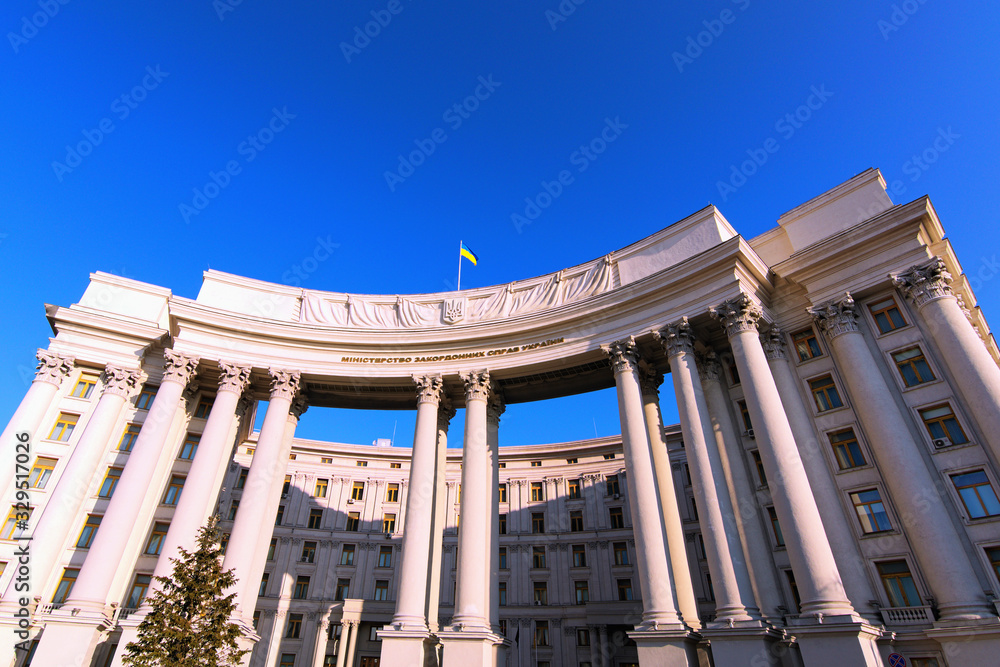 Wide-angle landscape view of building with columns of Ministry of Foreign Affairs of Ukraine against blue sky. Ukrainian Trident is coat of arms, Flag of the Ukraine on the top of the building