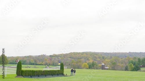 Men near steeplechase jump in distance before outdoor point-to-point horse race in autumn photo