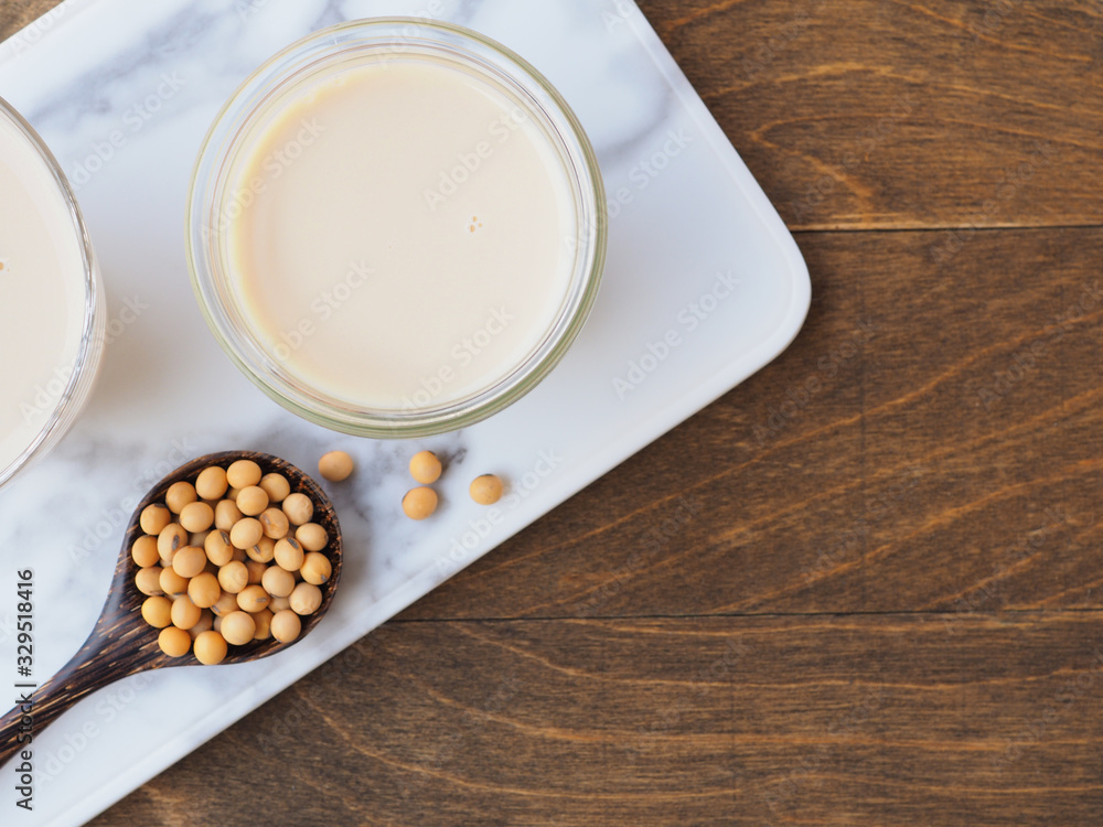 Soy milk in a glass cup with a wooden spoon on a white cutting board over wooden background. Top view with copy space. Plant protein. Soy milk in a glass cup with a wooden spoon on a white cutting board over wooden background. Top view with copy space. Plant protein.