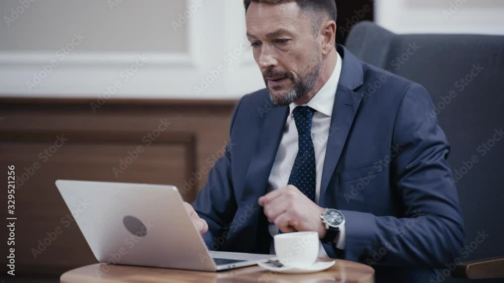 Businessman working on laptop and drinking coffee in lobby of restaurant Businessman working on laptop and drinking coffee in lobby of restaurant