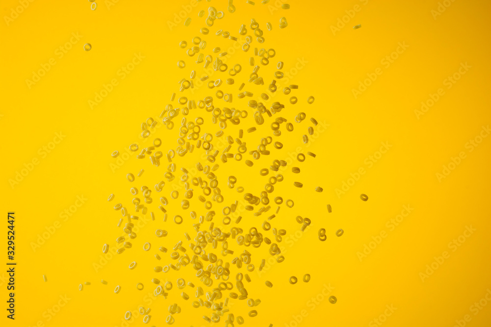 Freeze motion of flying uncooked pasta on yellow background, food concept