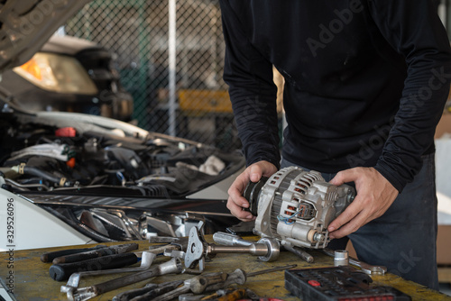Mechanic man holding alternator of the car on working table in repair and maintenance garage photo