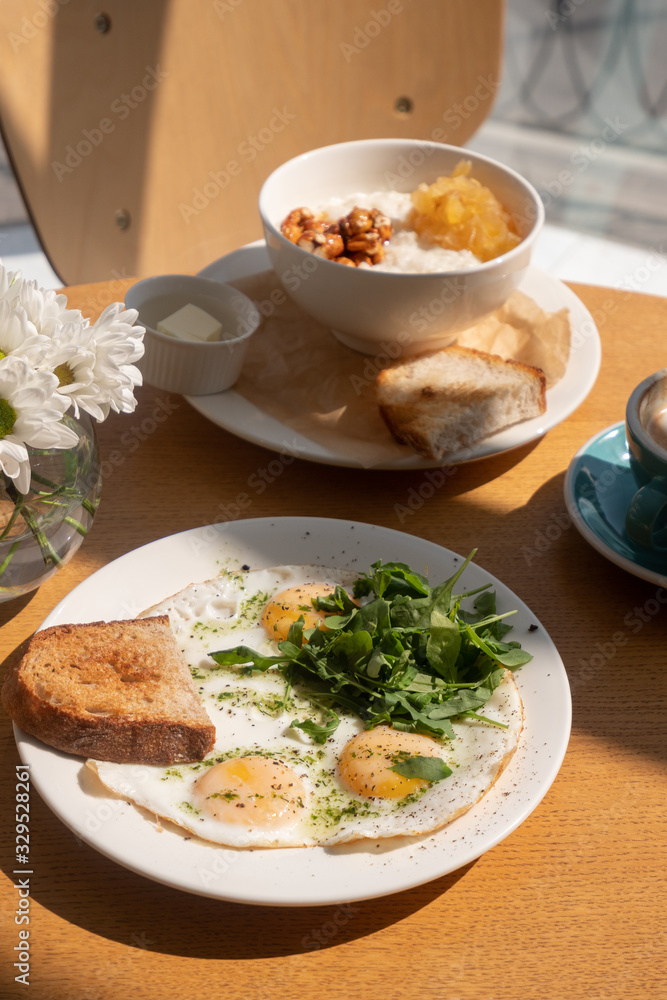 Tasty healthy breakfast: fried eggs, salmon, arugula and croutons on a white plate and a mug of cappuccino on a wooden table. Tasty healthy breakfast: fried eggs, salmon, arugula and croutons on a white plate and a mug of cappuccino on a wooden table.
