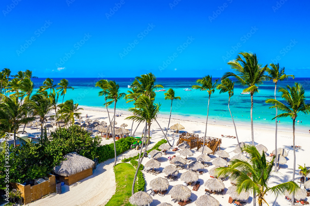 Naklejka premium Aerial drone view of beautiful atlantic tropical beach with palms, straw umbrellas and boats. Bavaro, Punta Cana, Dominican Republic. Vacation background.