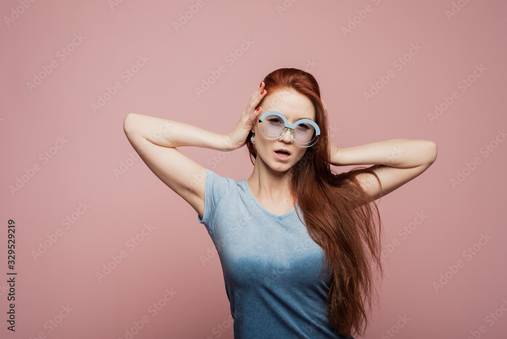 Stunning female model posing with joy face expression on pink background. Portrait of surprised young woman in sunglasses jumping in front of pink wall