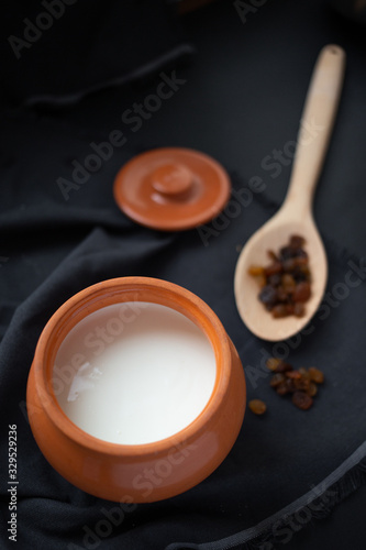 Brown pot with sour cream and a wooden spoon with raisins on a dark background.