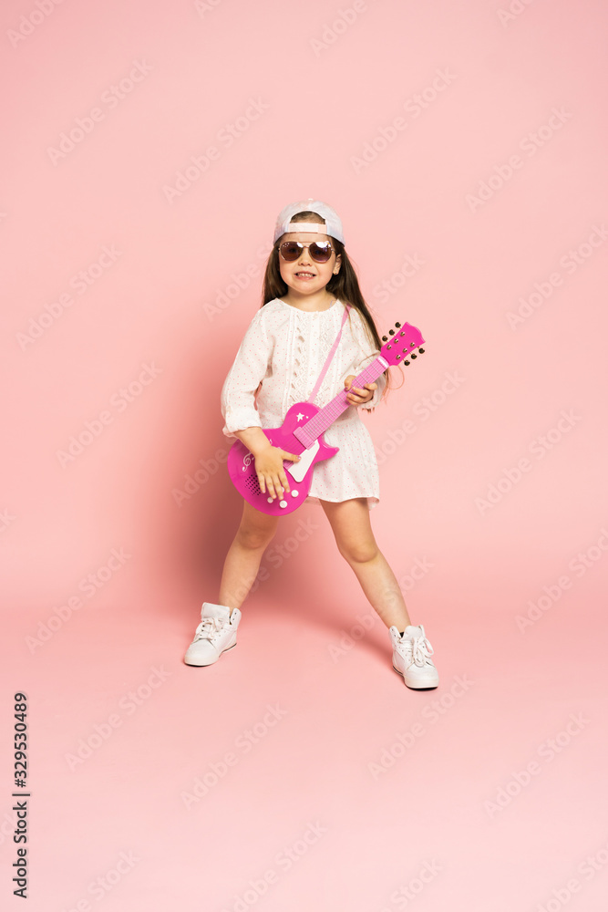 Laughing fashion little girl having fun with guitar isolated on pink background. Laughing fashion little girl having fun with guitar isolated on pink background.
