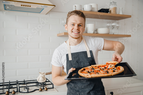 European man holds slice of fresh pizza on bright kitchen background