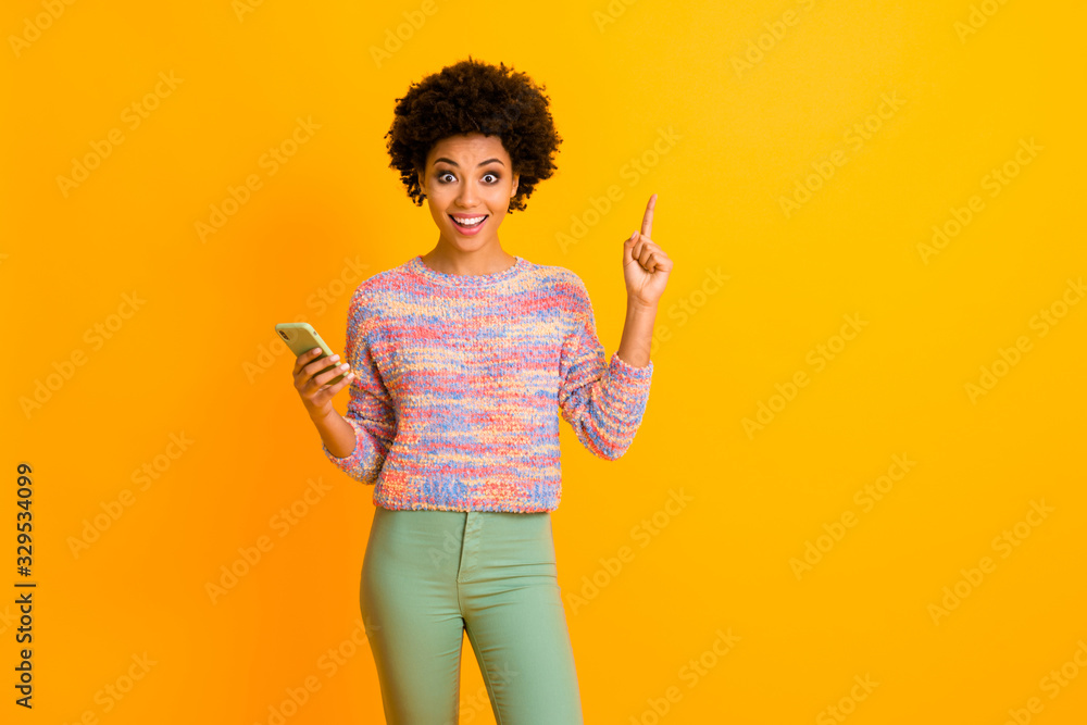 Portrait of crazy funky afro american girl use smart phone type post think impressed incredible idea scream wow omg raise finger up wear green pants trousers isolated bright color background Portrait of crazy funky afro american girl use smart phone type post think impressed incredible idea scream wow omg raise finger up wear green pants trousers isolated bright color background