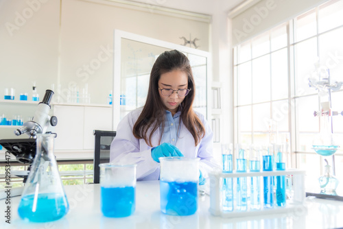 In a modern laboratory, a female chemist conducts experiments on the synthesis of compounds using a dropper and a solution in a test tube. COVID-19