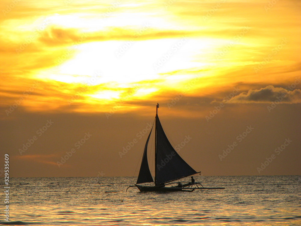 Fototapeta premium SILHOUETTE: Local Filipino person sails along a calm ocean at golden sunset.