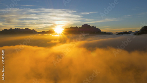 DRONE: Flying over clouds and a rocky ridge high in the French Alps at sunrise.