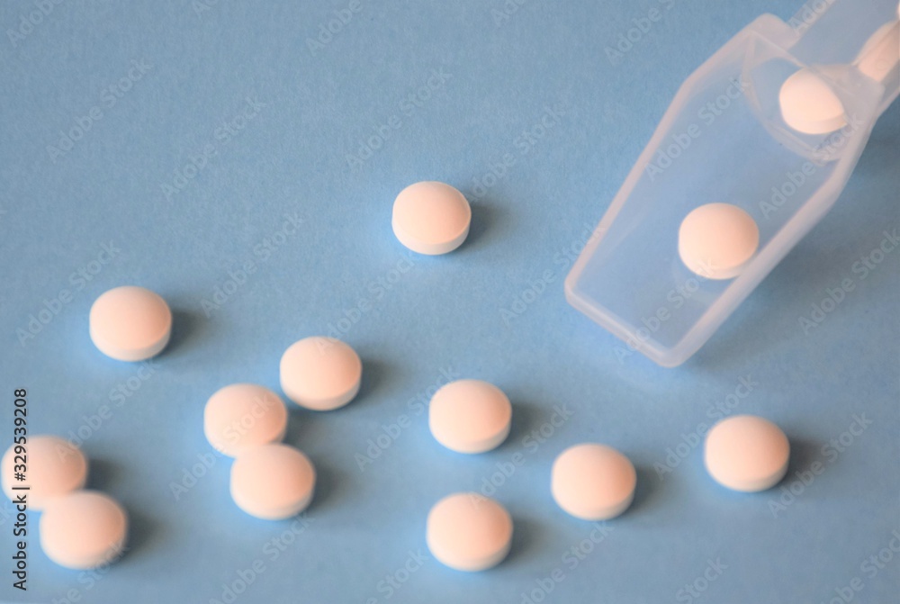 round white pills scattered on a blue background with a medical dispenser round white pills scattered on a blue background with a medical dispenser
