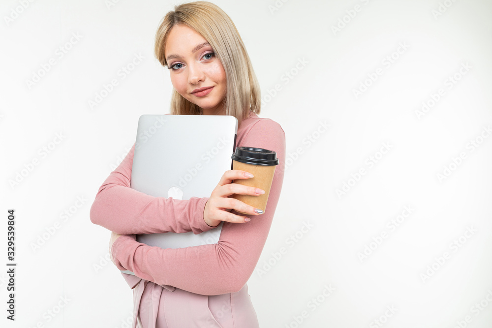 girl in pink stylish clothes and blond hair holding a cup of coffee and a laptop in her hands on a white studio background with copy space girl in pink stylish clothes and blond hair holding a cup of coffee and a laptop in her hands on a white studio background with copy space